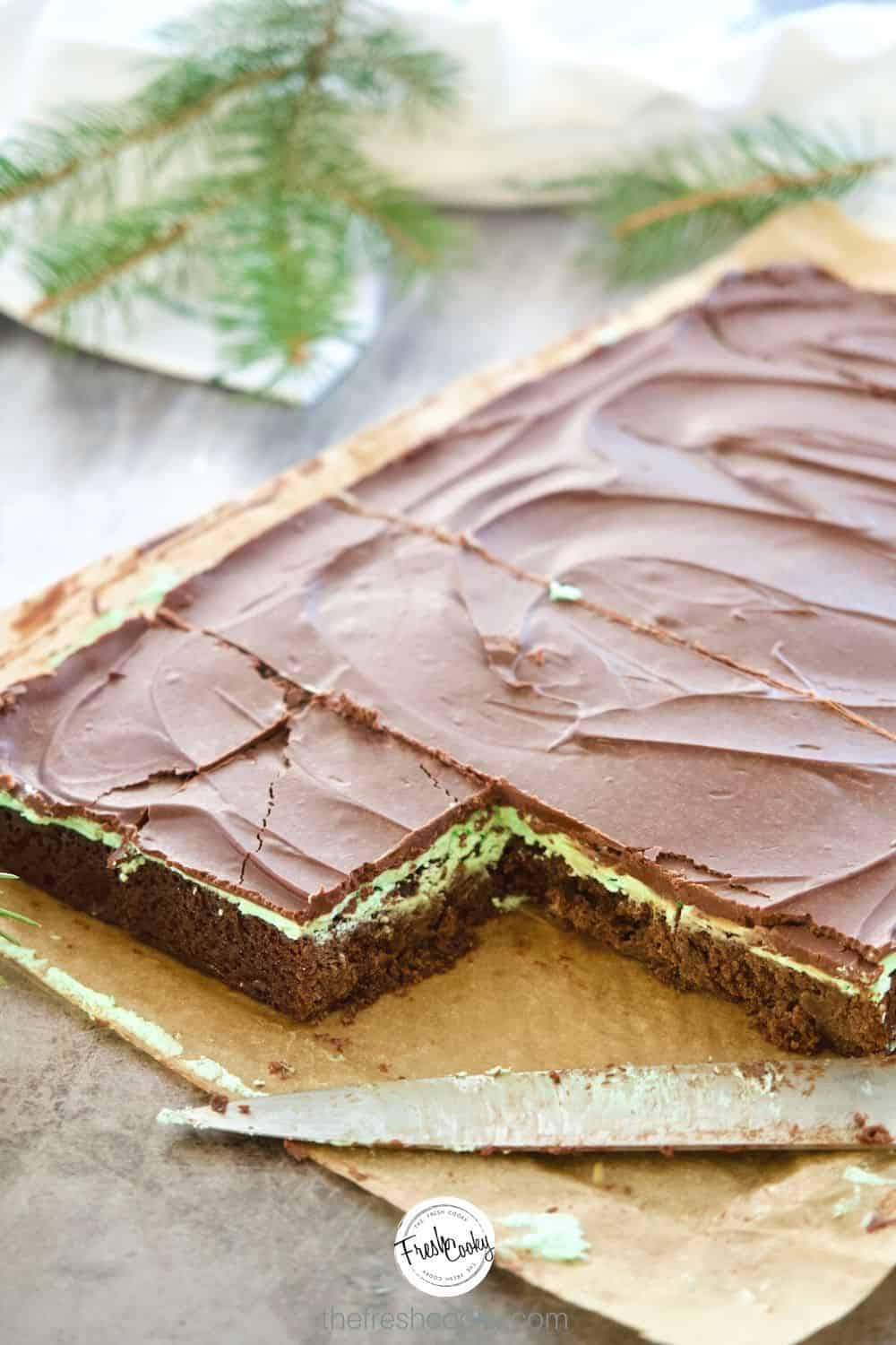 Sheet of triple layer mint fudge brownies, with two slices removed, knife in foreground on parchment paper.