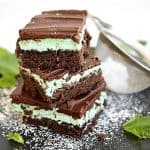 Image of 3 stacked chocolate fudge mint brownies, on a black plate with mint leaves and some powdered sugar.