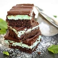 Image of 3 stacked chocolate fudge mint brownies, on a black plate with mint leaves and some powdered sugar.