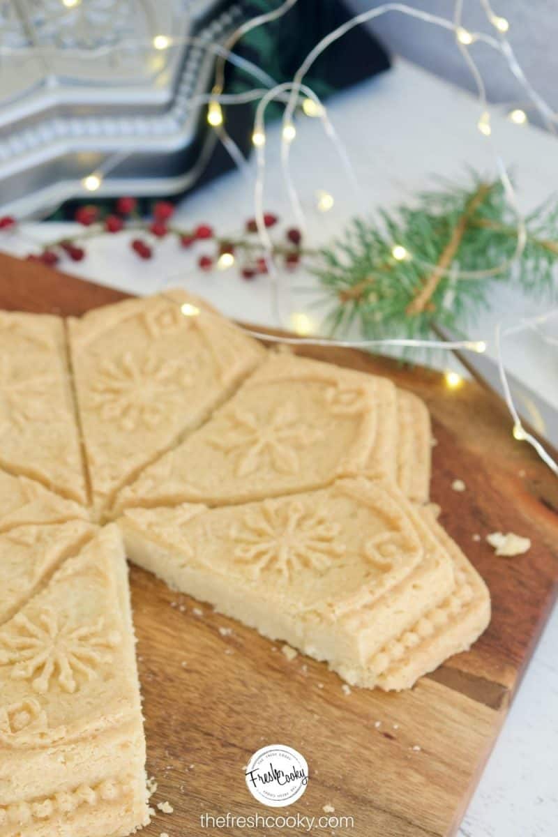 Molded Classic Shortbread Recipe using a snowflake mold, sitting on cutting board with twinkle lights and a sprig of evergreen
