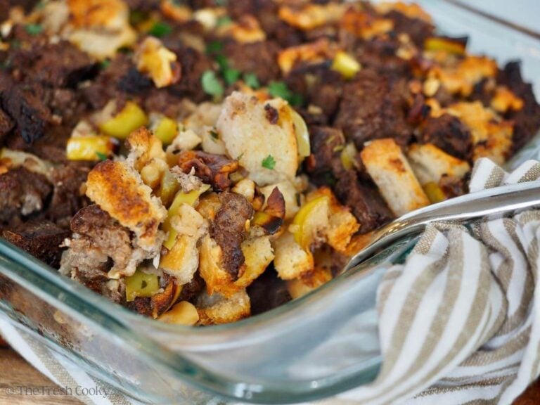 Sausage stuffing with pumpernickel bread and lots of veggies and apples in a glass baking dish.