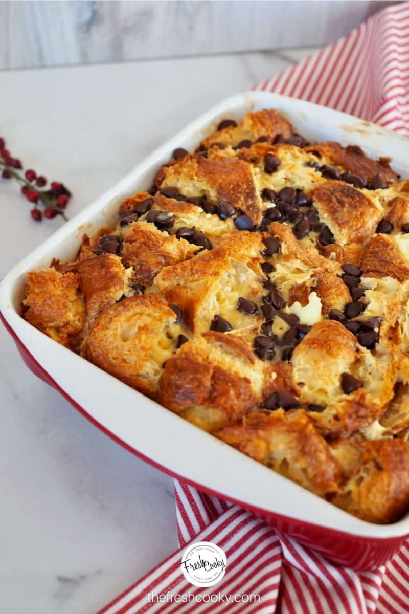 Image of square casserole baking dish on red striped towel filled with chocolate chip croissant french toast bake