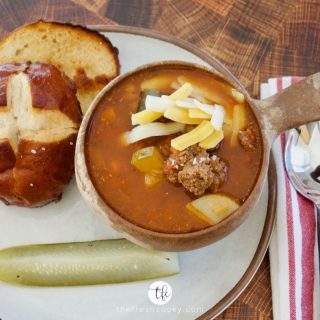 Facebook image of Healthy Cheeseburger Soup with pretzel bun and pickle on a plate.