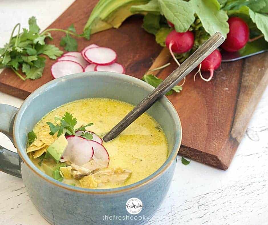 Facebook image for Creamy Chicken Poblano Soup in a rustic clay blue bowl with rustic soup spoon. with radishes on cutting board, fresh cilantro