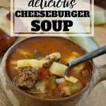 Pinterest image for healthy cheeseburger soup wiht image of bowl of soup with handle with ground beef, potatoes, pickles in the background.