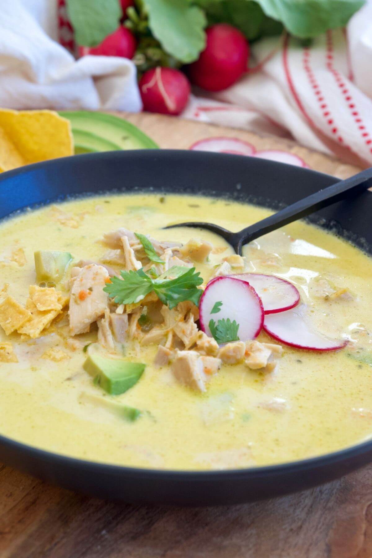 Cream of poblano soup in black bowl with a spoon, brothy, light and full of chicken and veggies. 