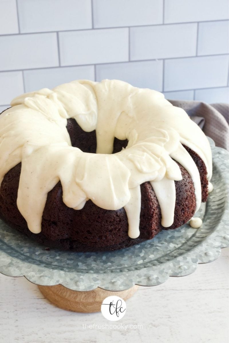 Image of chocolate cake topped with vanilla buttercream glaze, sitting on top of a galvanized cake stand