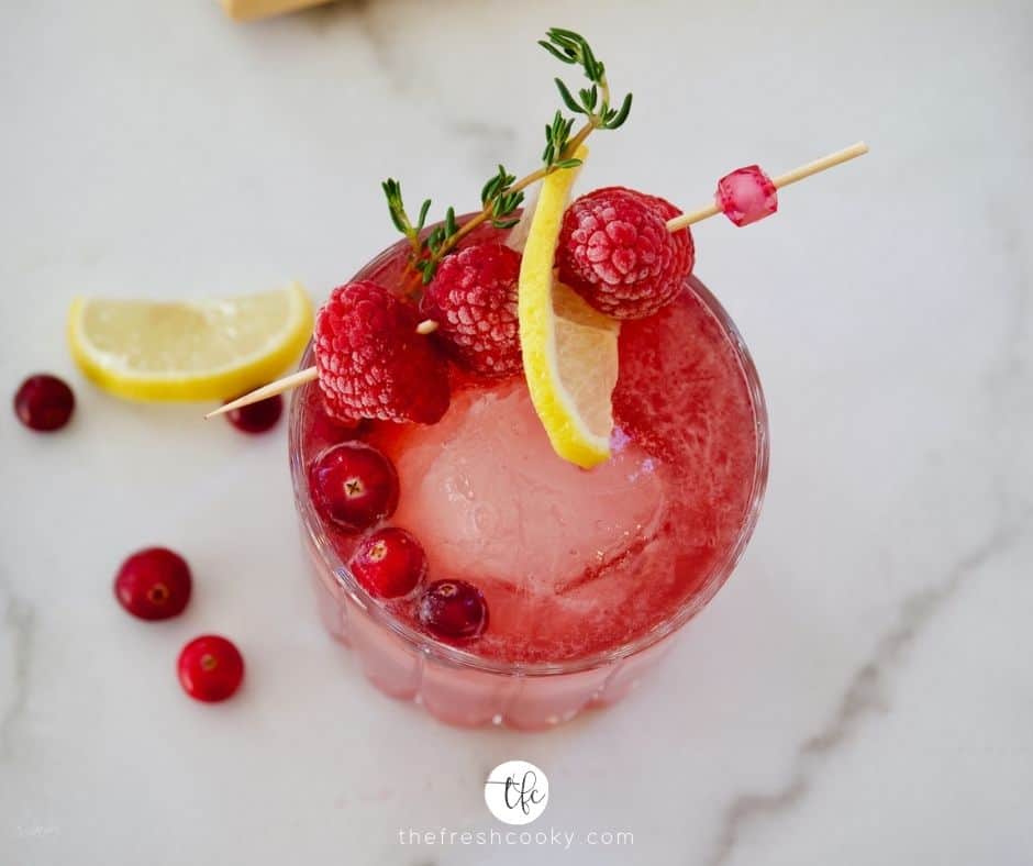 Top down image of Cranberry Bourbon Sour on marble with raspberries garnish, sprig of thyme and lemon