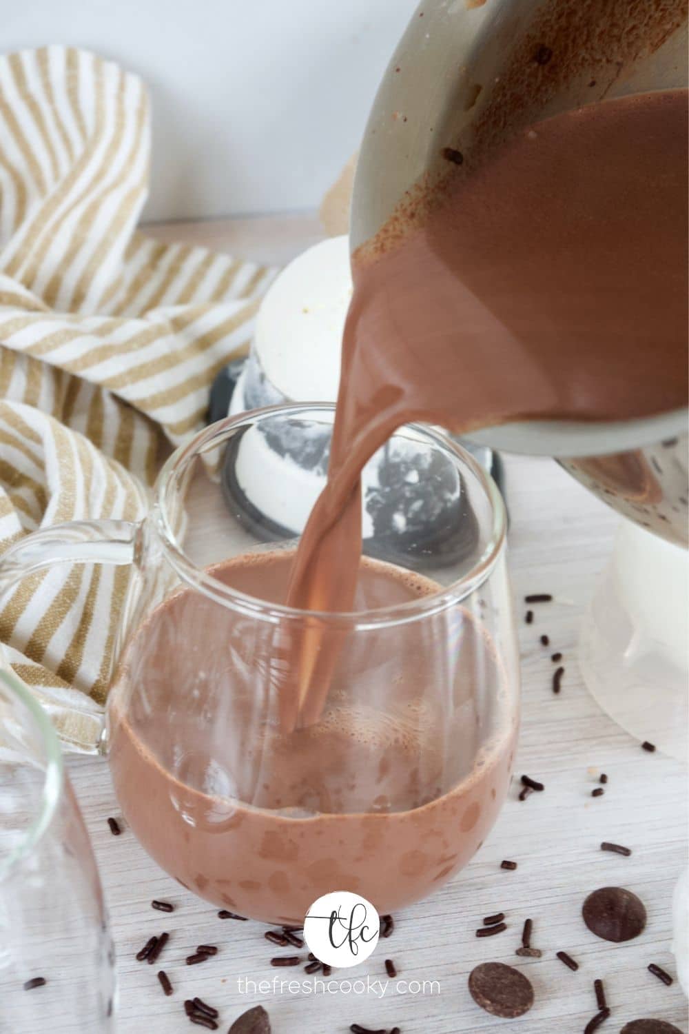 A small saucepan pouring homemade hot chocolate into a glass mug.