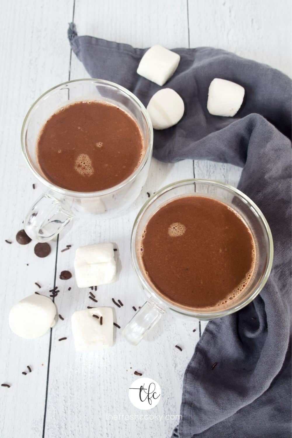 Overhead shot of homemade hot chocolate in glass mugs with a blue napkin and marshmallows.