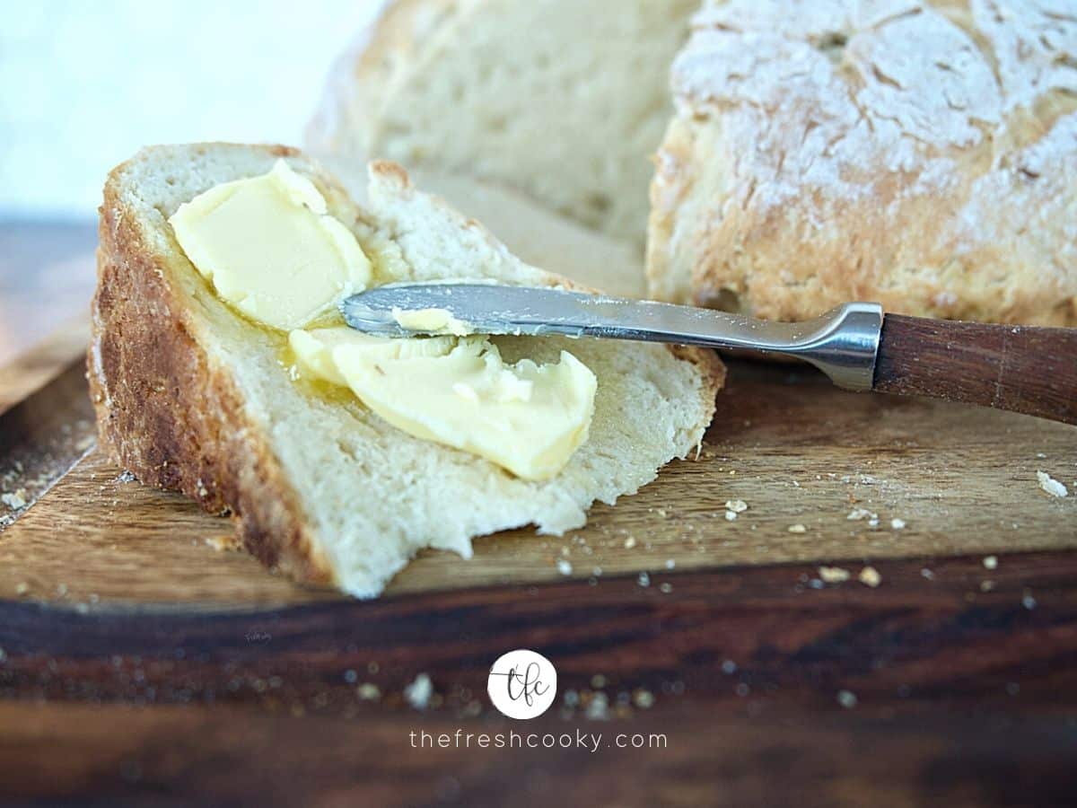 Close up shot of butter spreading on wedge of Irish Soda bread with loaf in background.
