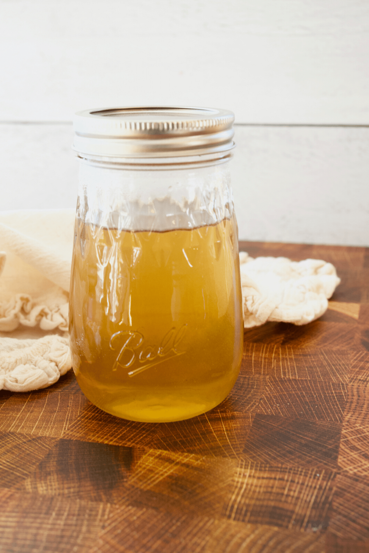 Liquid Cane sugar in glass jar with canning lid on top, off white napkin behind on cutting board.