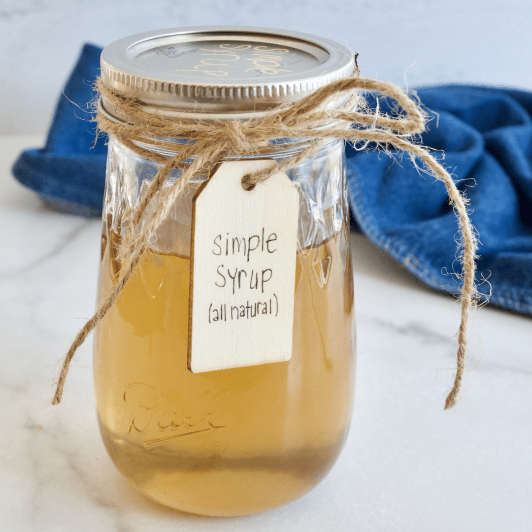 Liquid cane sugar in jar with lid, a golden liquid, tied with jute and labeled simple syrup, all natural.