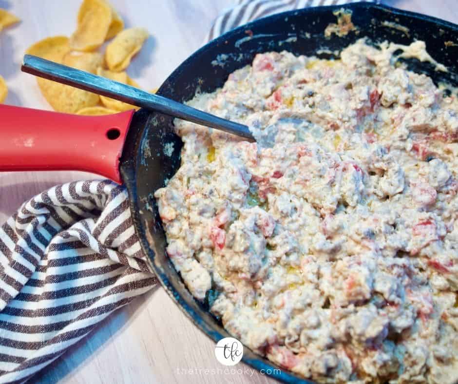 creamy sausage cream cheese dip in cast iron pan on counter with black spoon, scoops in background.