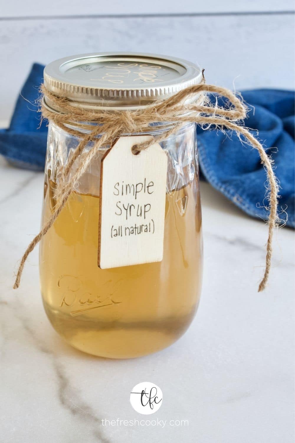 A mason jar filled with a golden amber cane sugar simple syrup, tied with twine and a label.