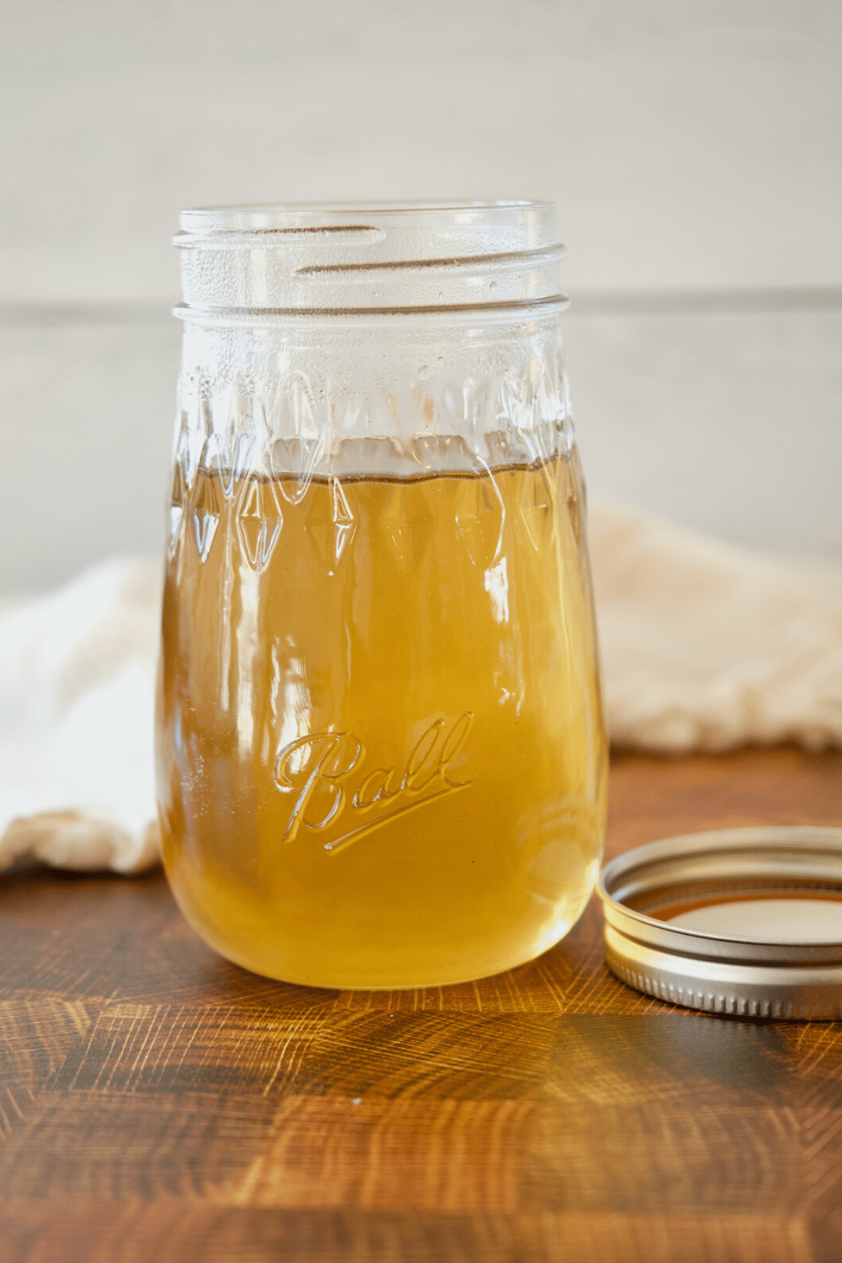 Cane sugar syrup, cooling in open glass ball jar on wood counter with lid nearby.