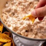 Sausage dip in skillet, hand scooping with a chip.