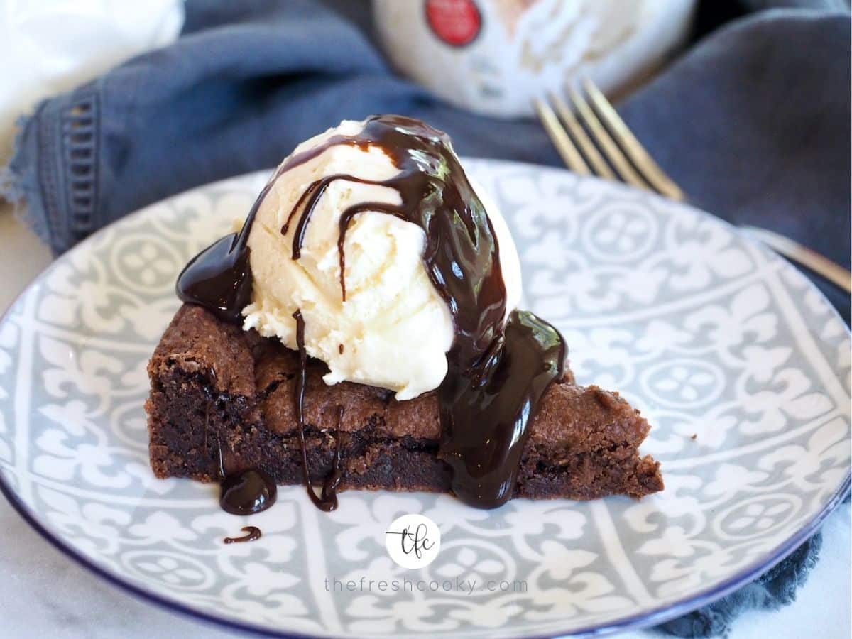 Chocolate shortcake cake on a plate with scoop of vanilla ice cream and chocolate fudge drizzled on top.