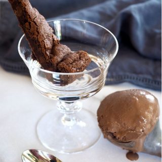 Wedge of Chocolate Shortcake in glass footed bowl with chocolate ice cream in ice cream scoop on table.