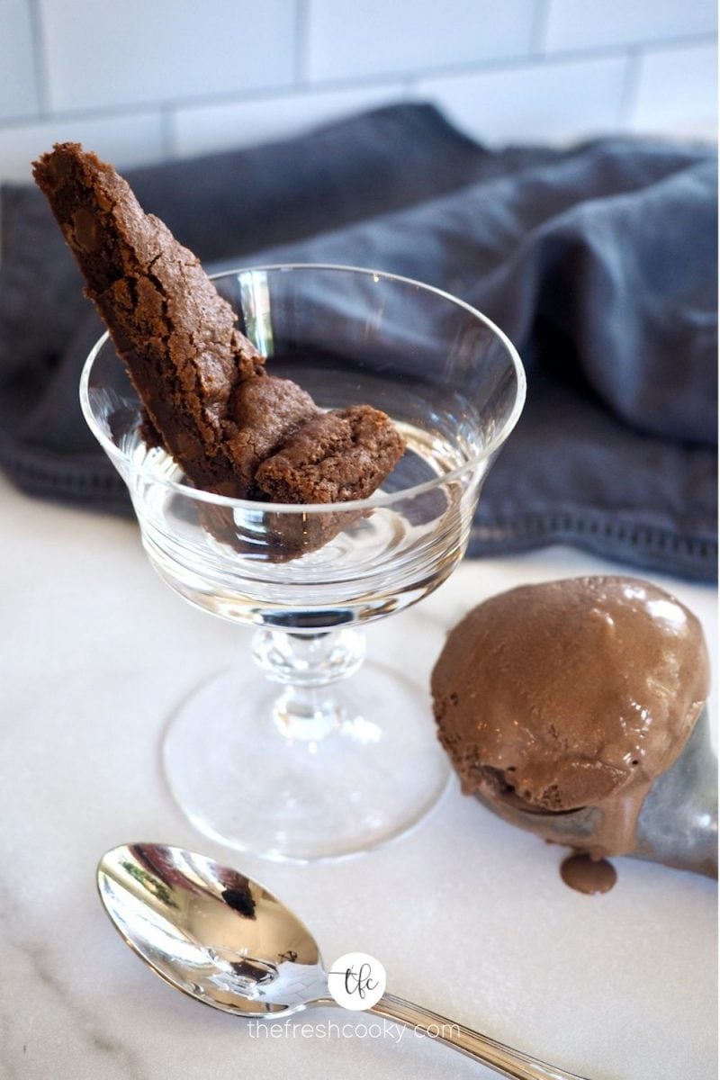 Wedge of Chocolate Shortcake in glass footed bowl with chocolate ice cream in ice cream scoop on table.