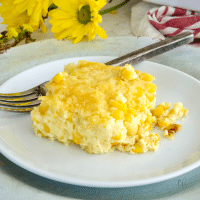Square image for corn pudding casserole with square of corn pudding on a plate with a fork and yellow flowers behind.