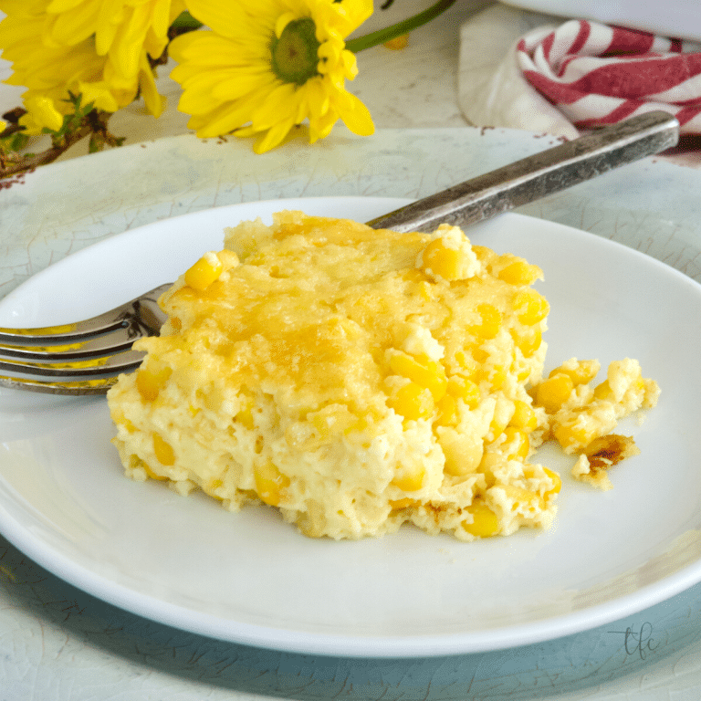 Square image for corn pudding casserole with square of corn pudding on a plate with a fork and yellow flowers behind.