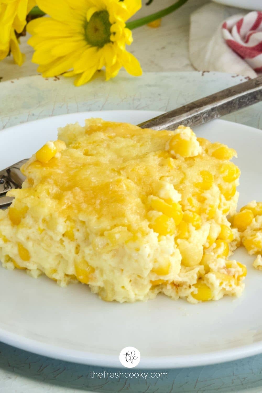 A serving of the best corn pudding casserole without jiffy mix on a pretty plate with yellow daisies in background.