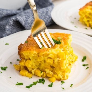 Corn pudding casserole on plate with fork stuck in it.