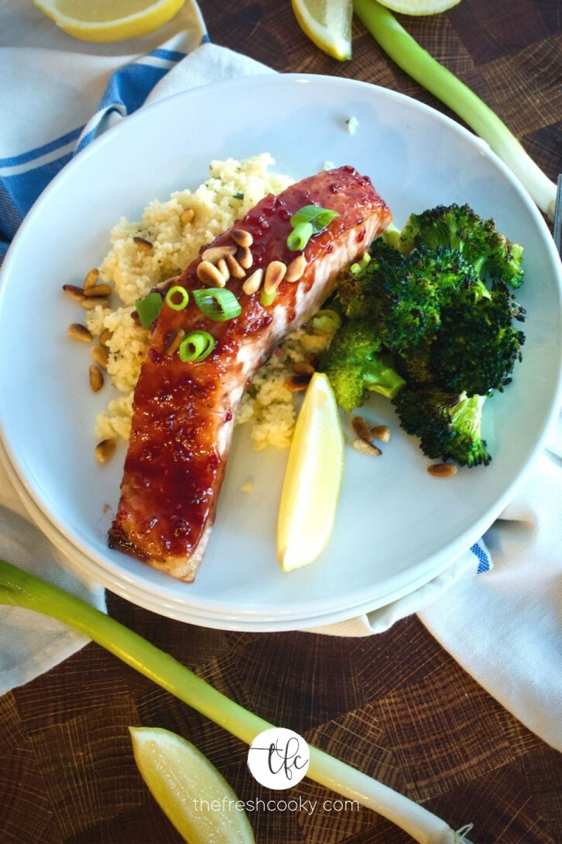 Plate with raspberry glazed salmon fillet on a bed of couscous with roasted broccoli and lemon wedge.
