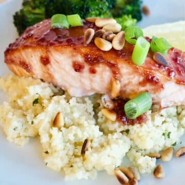 healthy raspberry glazed salmon on a bed of couscous with roasted broccoli in background.