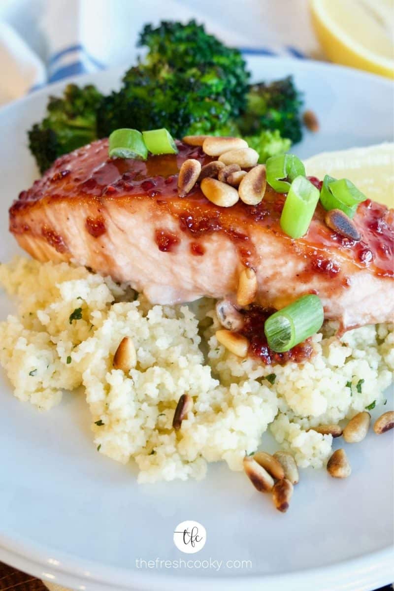 healthy raspberry glazed salmon on a bed of couscous with roasted broccoli in background.