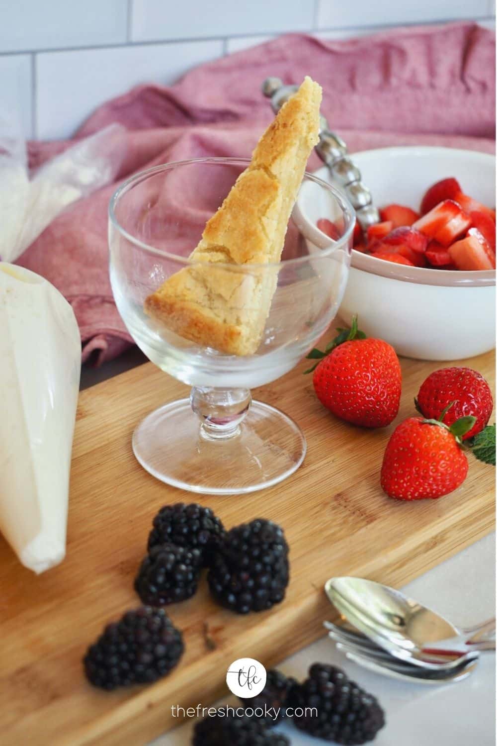 Shortcake sliced into wedge or triangle in pretty glass dish with strawberries and whipped cream ready to assemble.