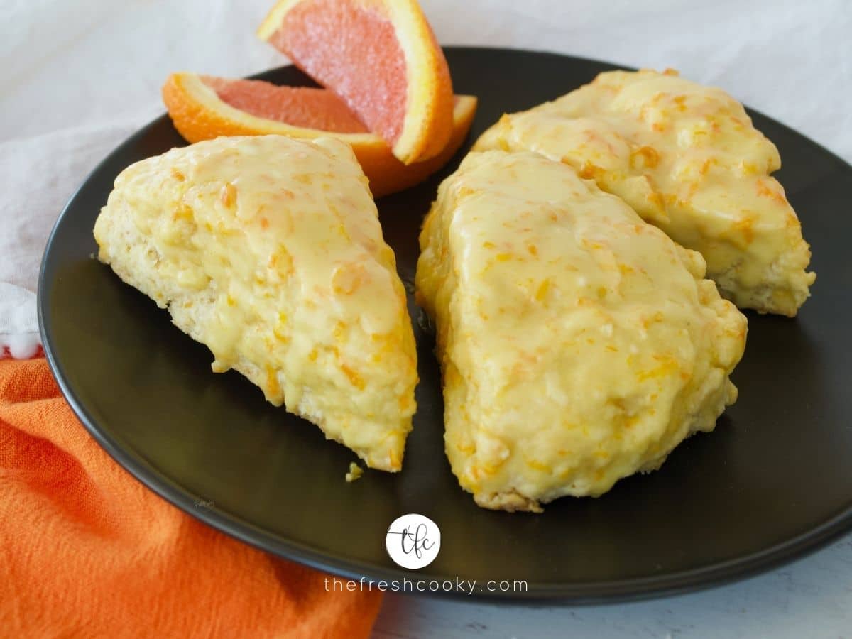 FB image for panera orange scones on a black plate with orange napkin and three scones with a couple of orange slices.