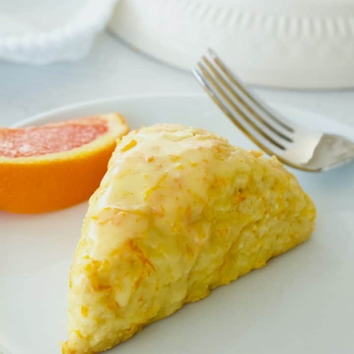 Image of orange scone on white plate with wedge of orange and fork.