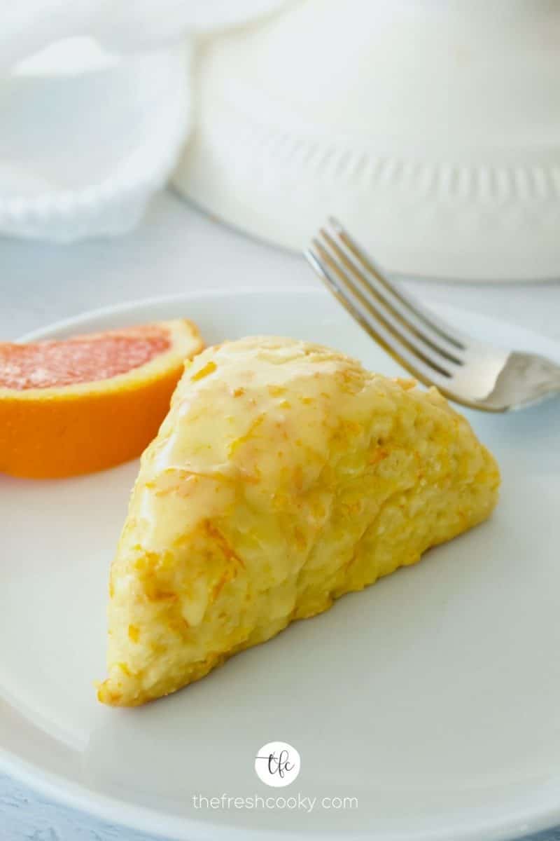 Image of orange scone on white plate with wedge of orange and fork.
