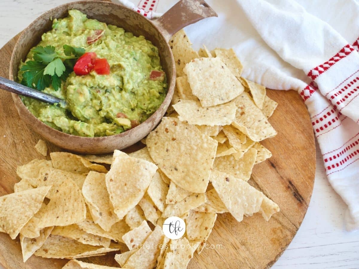 Facebook image for super simple guacamole on a wooden tray with tortilla chips and spoon in bowl of guacamole.