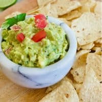 marble bowl filled with homemade guacamole on a wooden tray with tortilla chips.