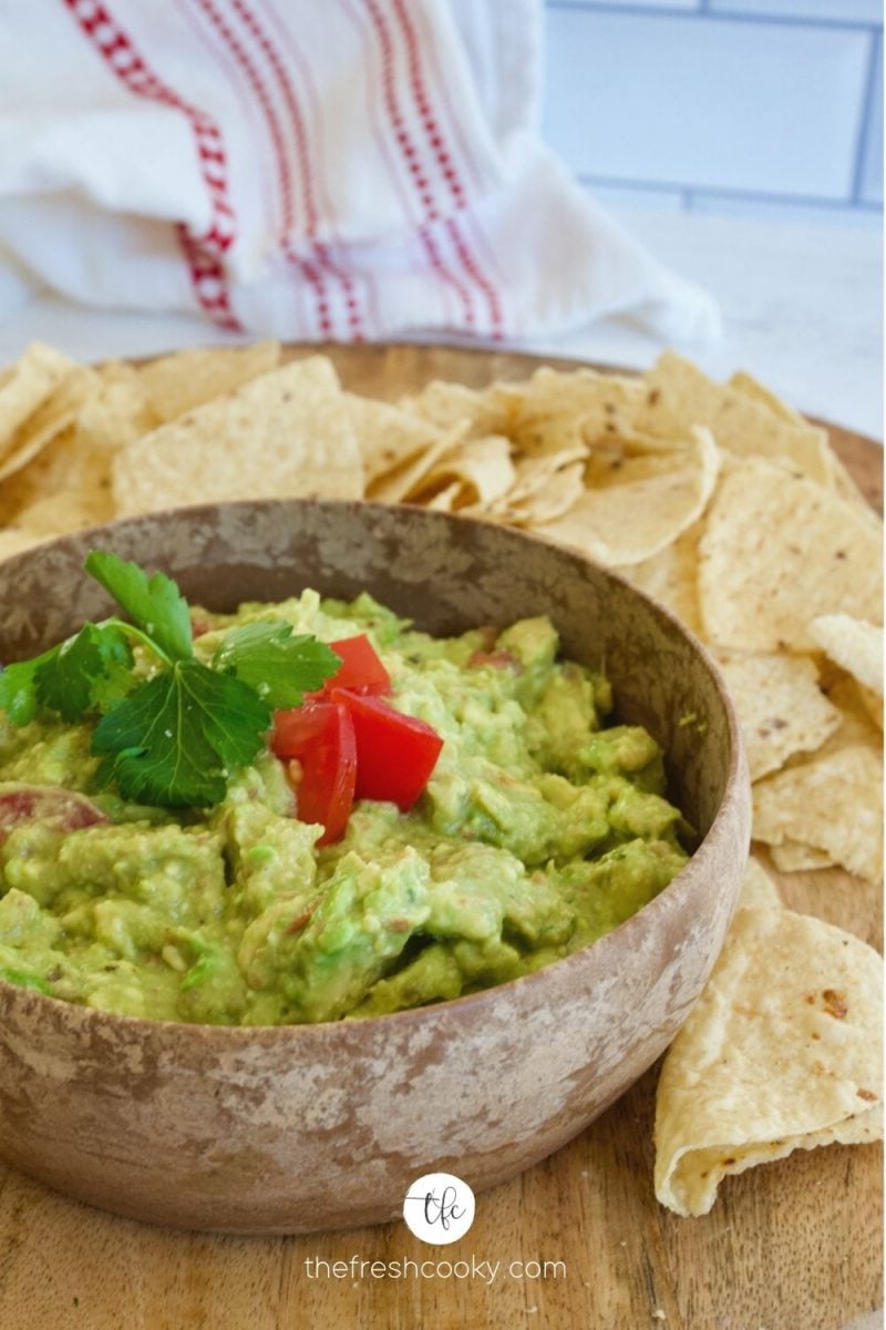 Fresh homemade simple guacamole in a wooden bowl on a tray with fresh tortilla chips.