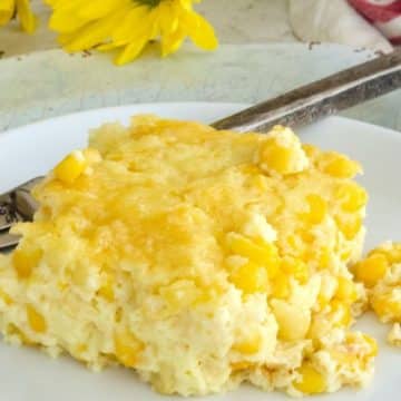 A serving of the best corn pudding casserole without jiffy mix on a pretty plate with yellow daisies in background.