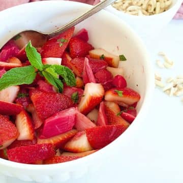 Bowl filled with Strawberry Rhubarb Salad with almonds in the background for tossing.
