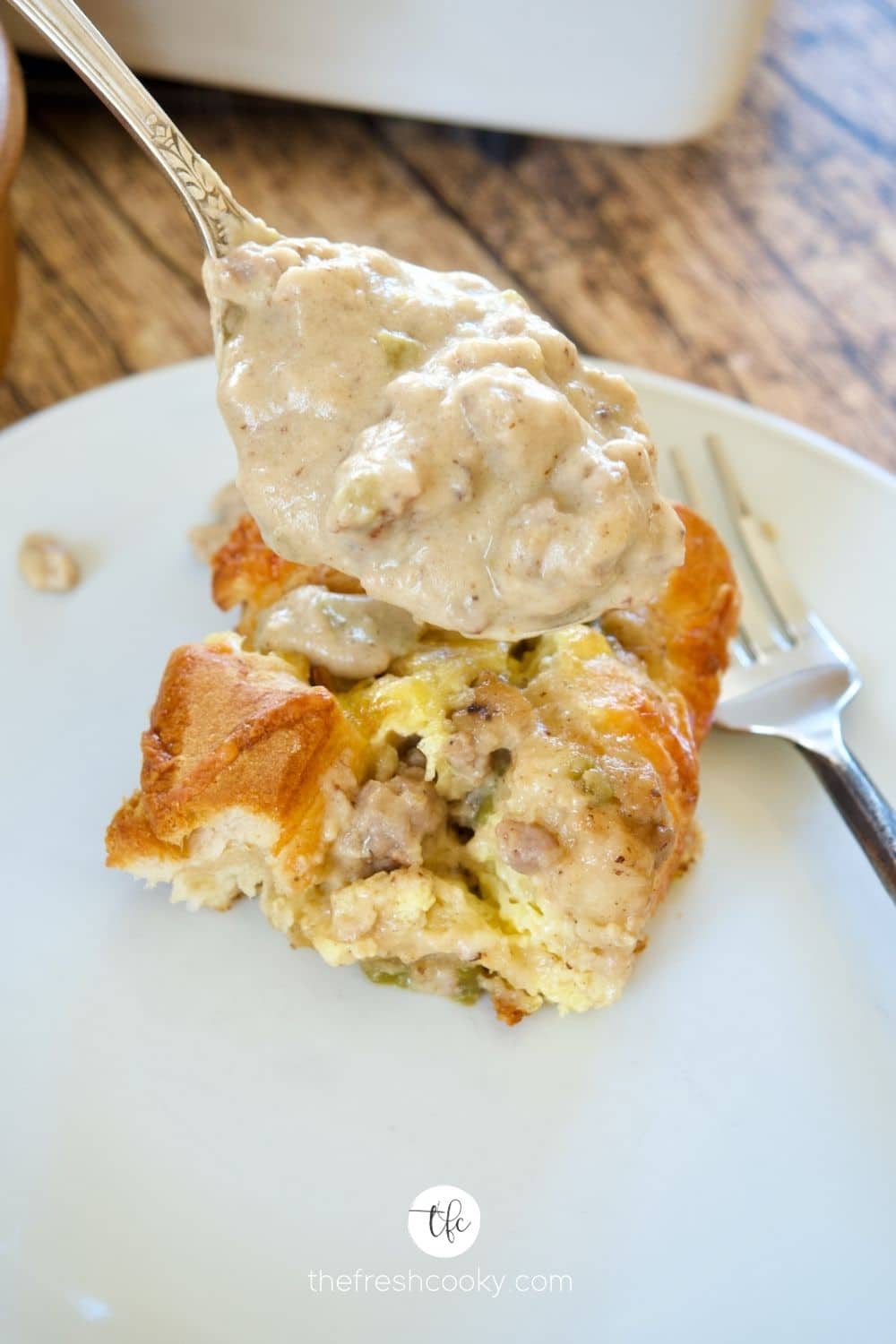 Spooning sausage gravy over a slice of biscuits and gravy egg bake.