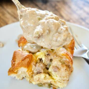 Breakfast Casserole slice on plate with spoonful of sausage gravy being poured over the top.