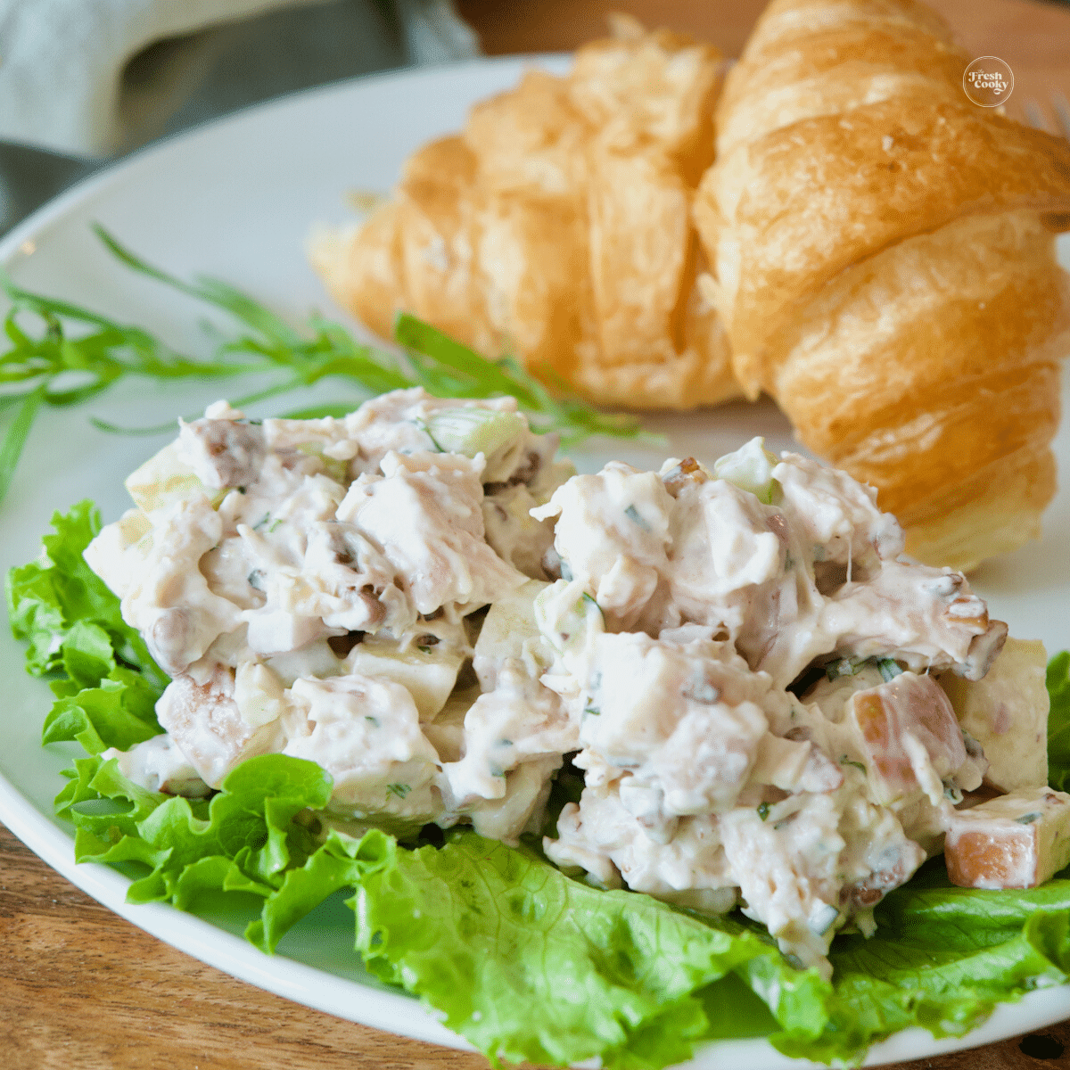 Pecan apple chicken salad on bed of lettuce with croissants behind.