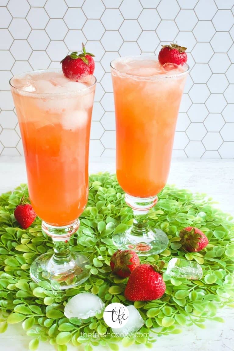 Two pretty tall glasses with strawberry gin and tonic on bed of fake leaves with strawberries and ice cubes.