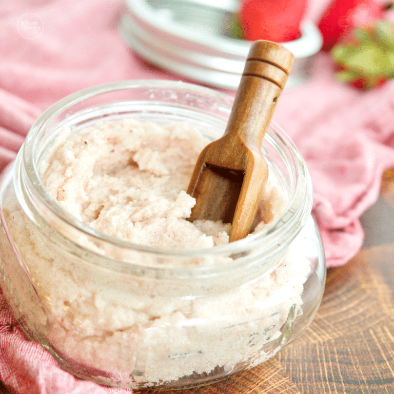 Image of glass jar of Whipped Sugar Scrub Soap recipe with scoop, strawberries in the back.