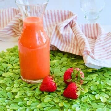 Strawberry simple syrup in a jar with fresh strawberries.