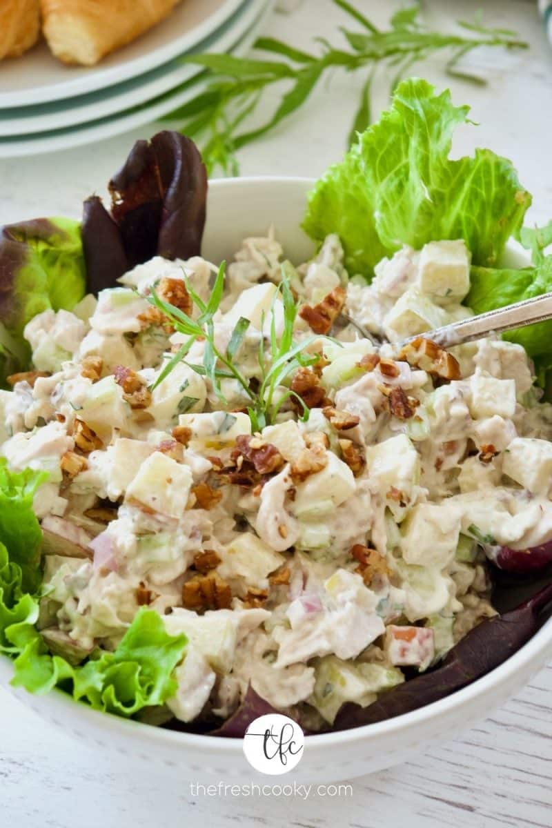 Tarragon Chicken Salad in bowl lined with red and green lettuce leaves, with croissants on a plate behind.