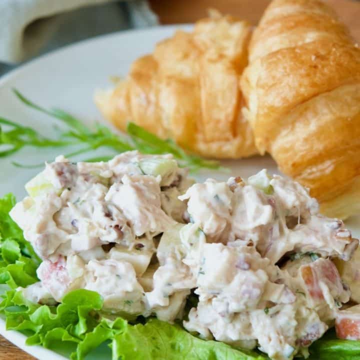 Tarragon Chicken Salad on a bed of lettuce with croissants behind.