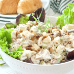 Bowl filled with butter lettuce and chunky, creamy tarragon chicken salad with croissants in background.