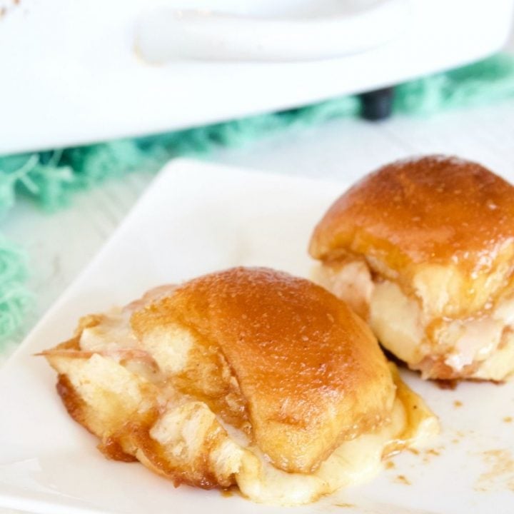 Two gooey Turkey and Cheese Sliders on white plate with casserole behind.